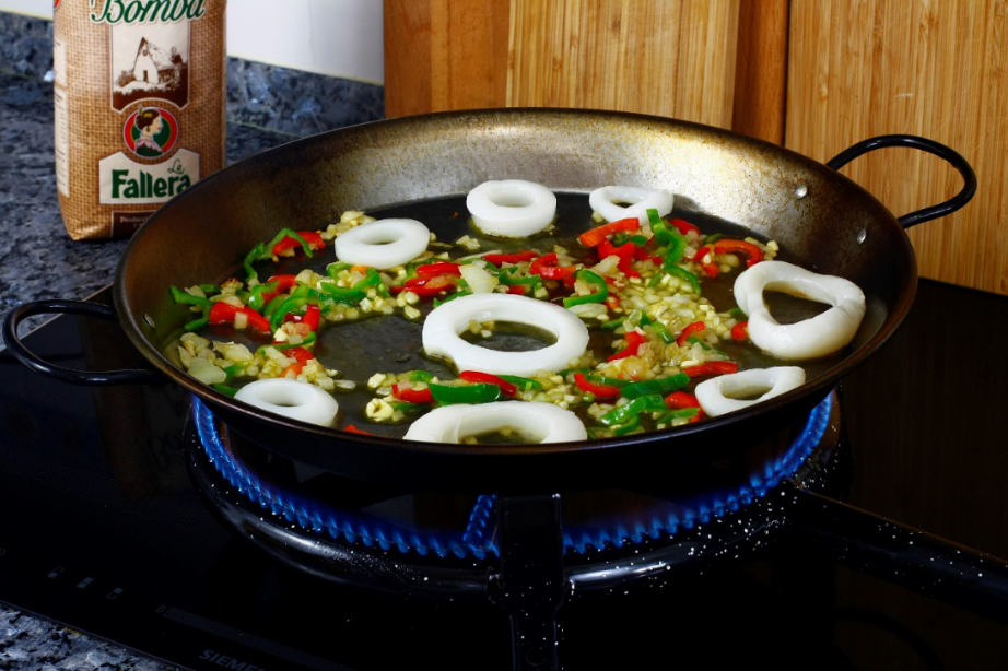 En una paella, añadimos el ajo, la cebolla, el pimiento rojo y el pimiento verde.