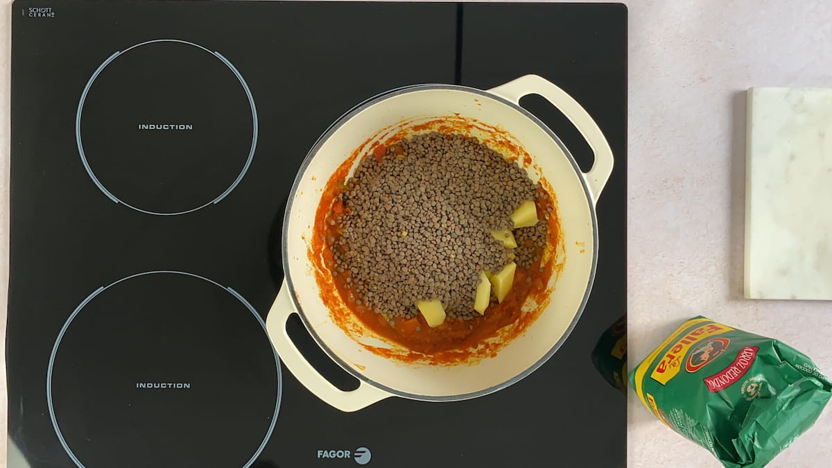 Receta lentejas con arroz paso 4 añadimos el tomate triturado a nuestra mezcla y dejamos que evapore el agua. Incorporamos las patatas chascadas y las lentejas y rehogamos unos minuto