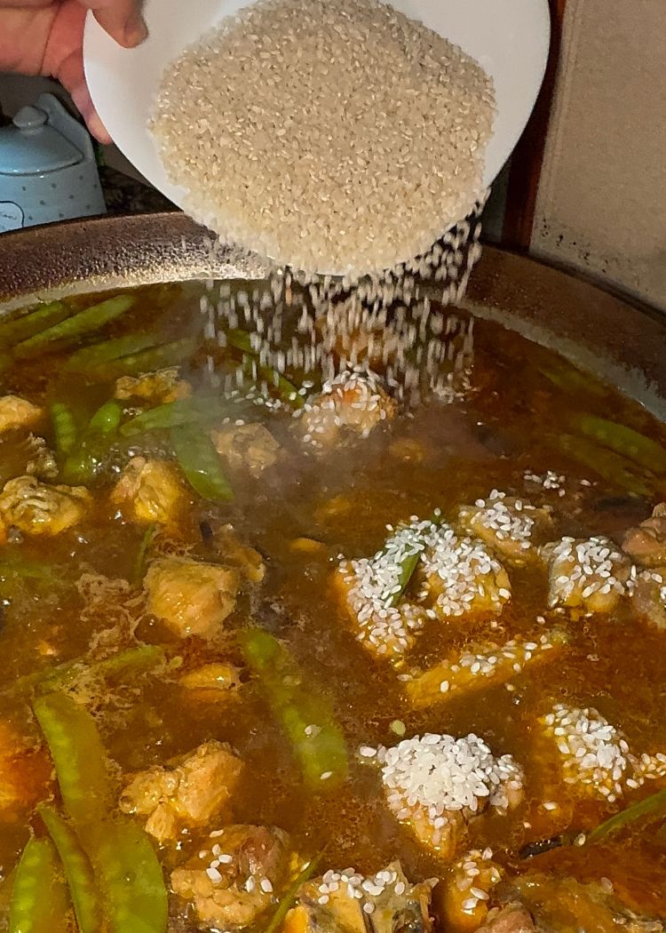 Añadir arroz a paella de pollo y verduras